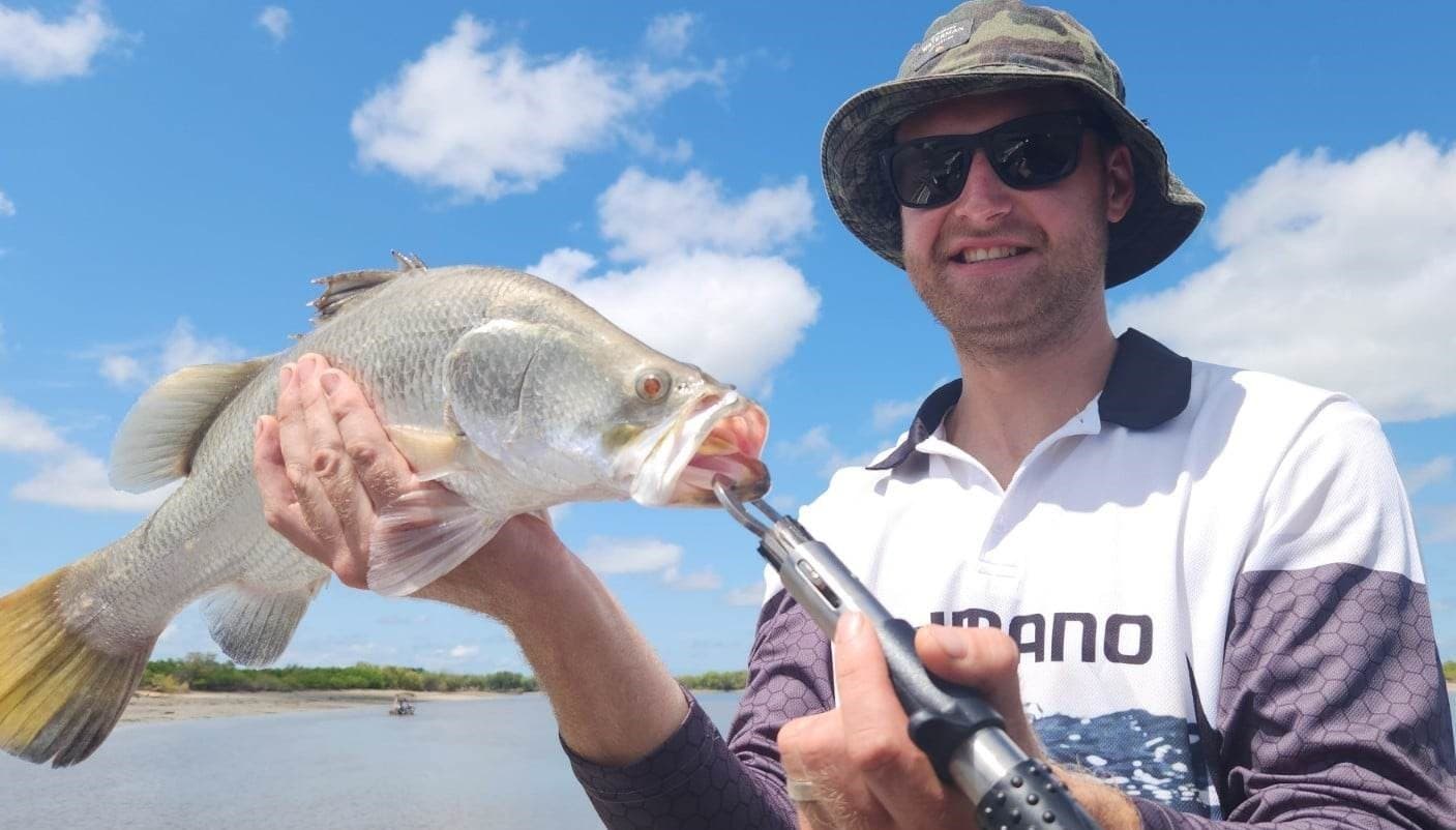 Fisherman gripping barramundi with lip-grip tool on sunny river trip