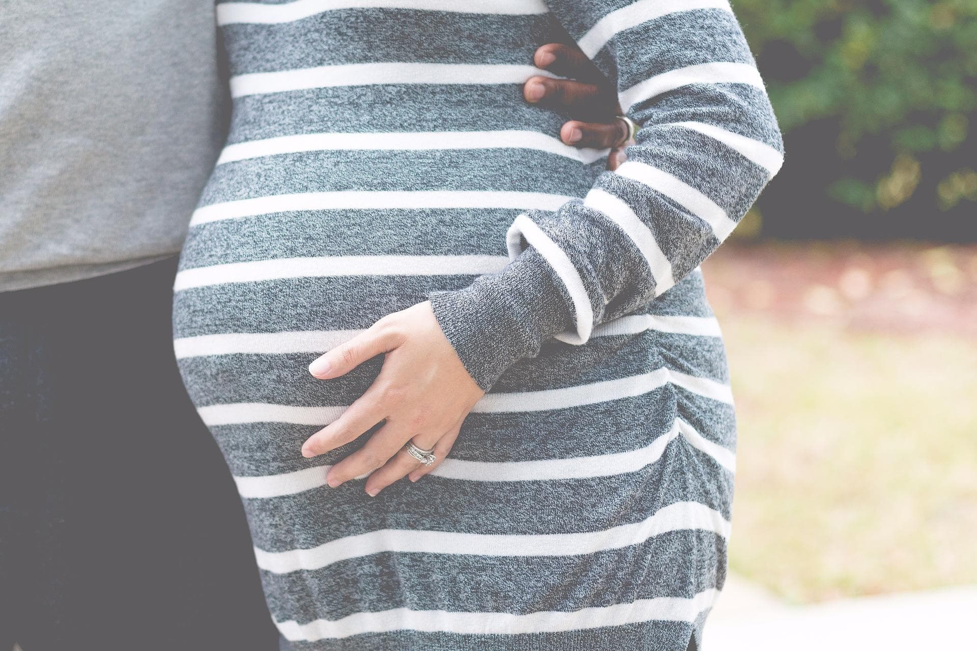 Pregnant woman outdoors in striped dress showing baby bump