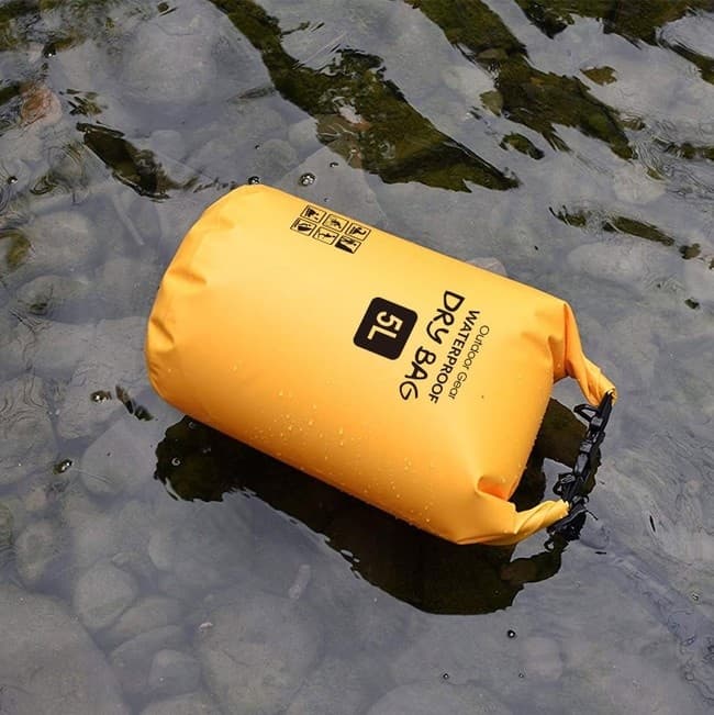 Yellow dry bag floating on river stones, waterproof gear shot