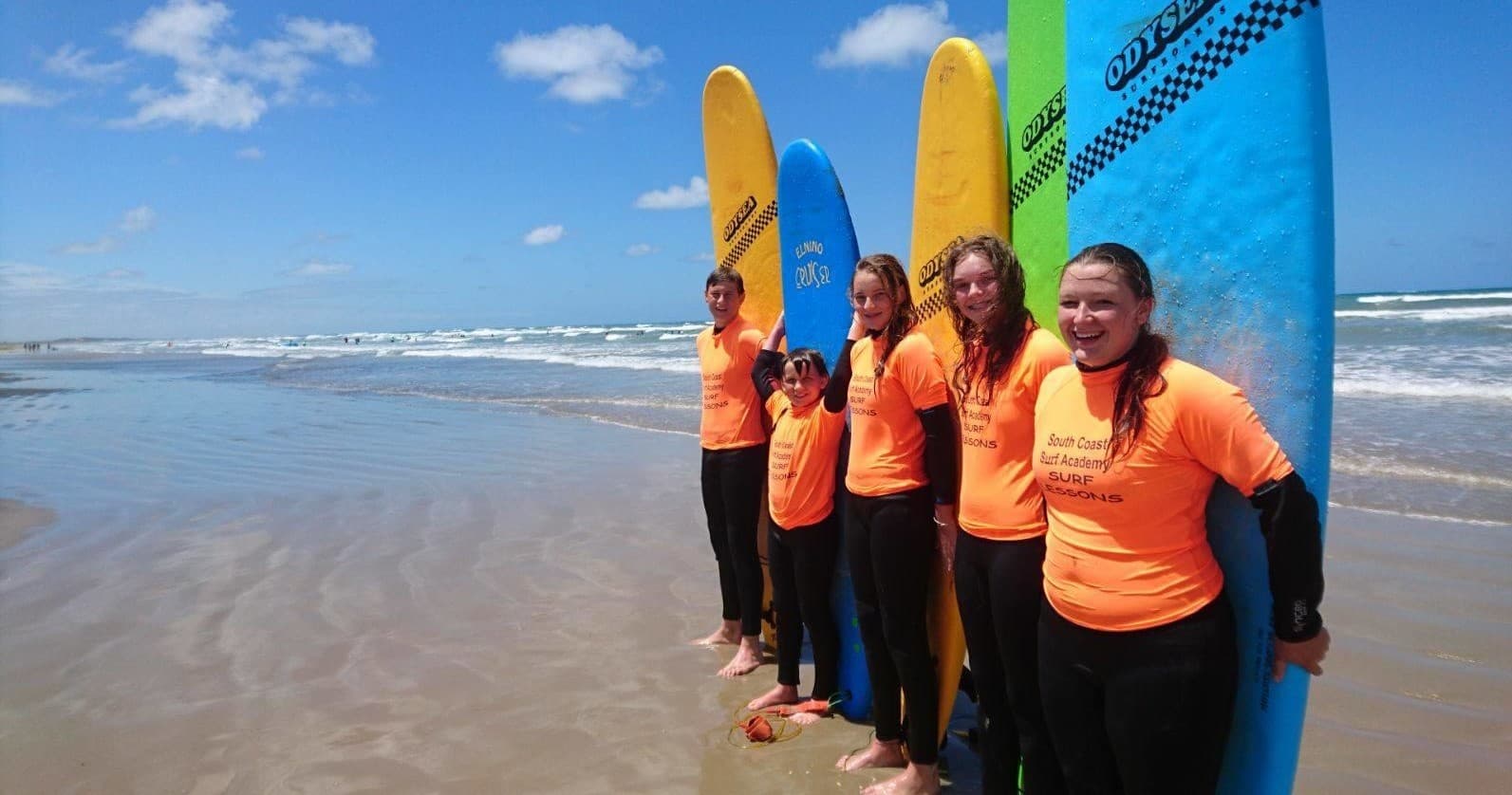 Surf students standing with colorful boards on sandy beach