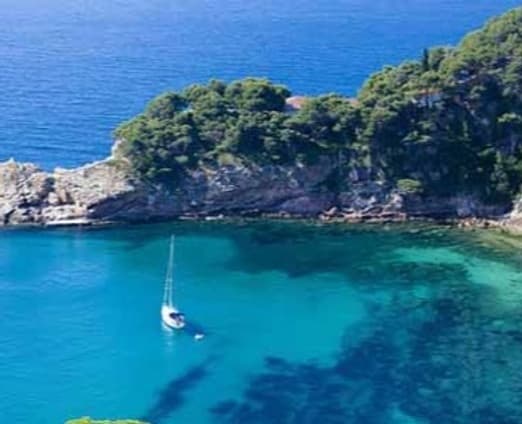 Sailboat anchored in turquoise coastal cove by rocky shoreline
