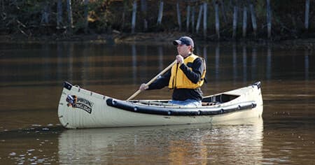 Solo canoeist paddling along forested river at golden light