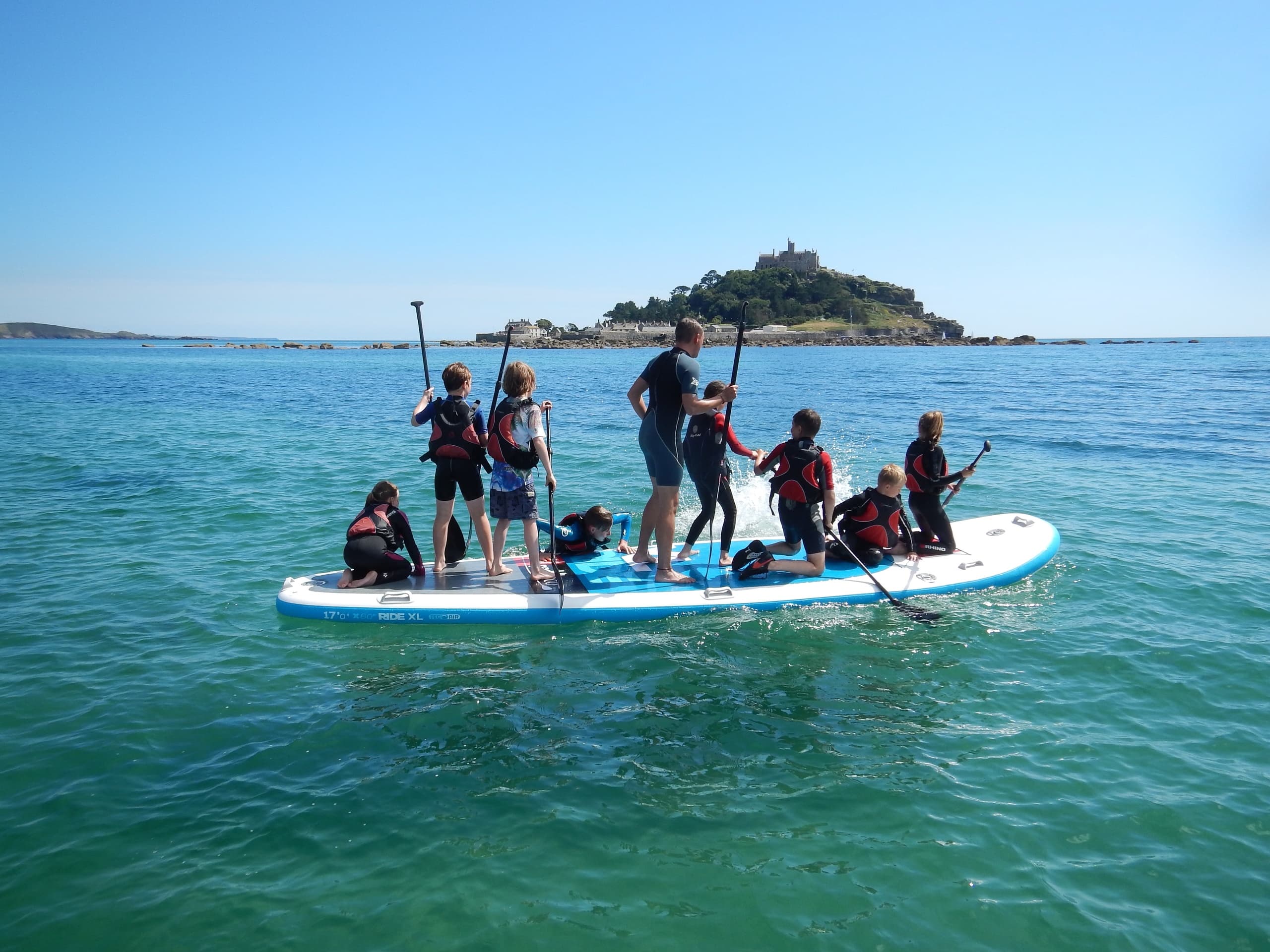 Large group stand-up paddleboarding on calm sea with island