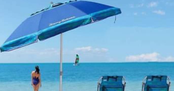Beach umbrella shading chairs on sandy shore, expansive ocean view