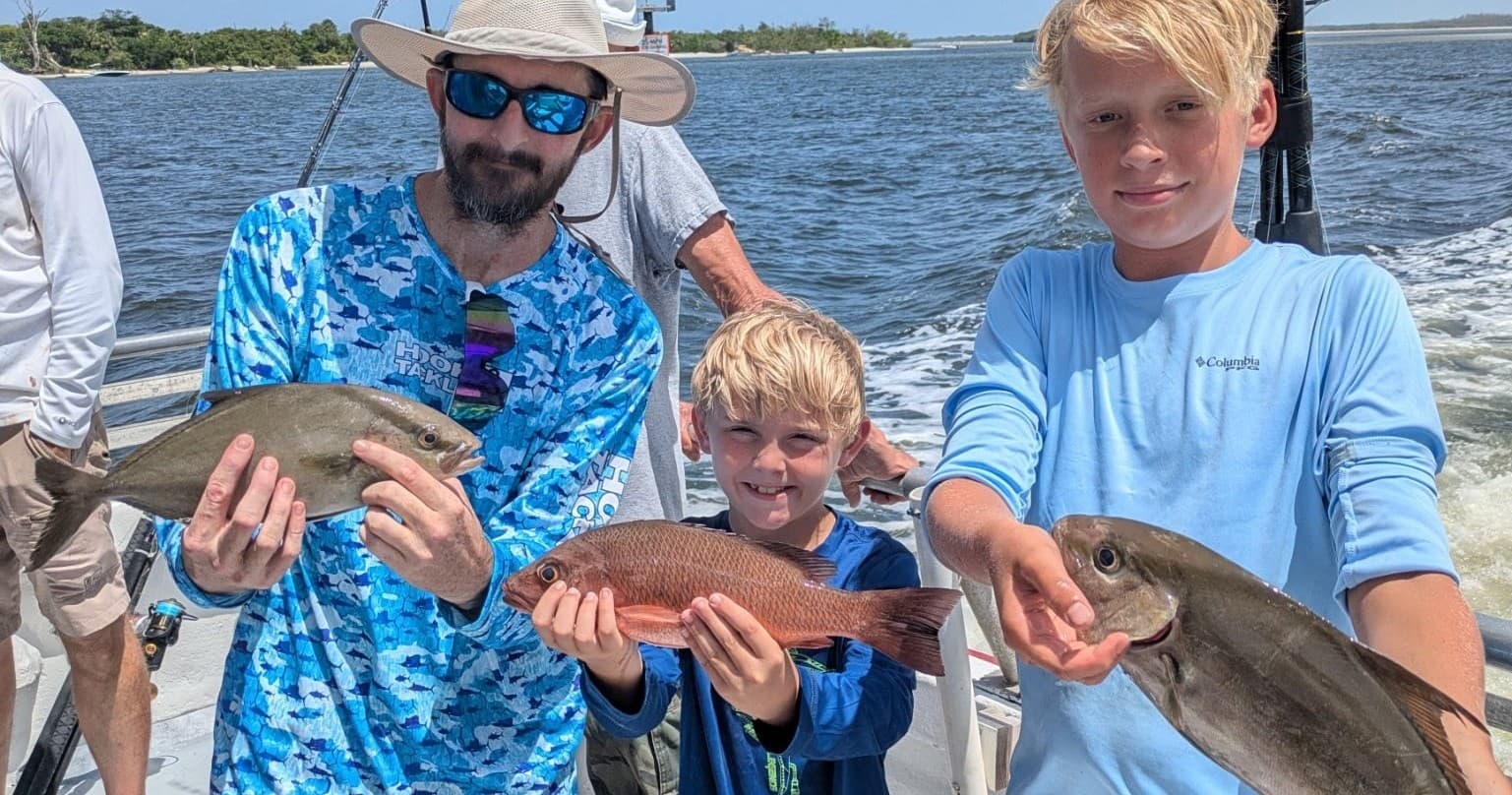 Family fishing trip with kids holding reef fish aboard coastal charter