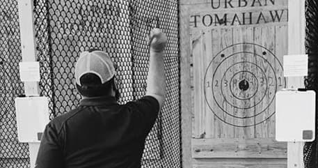 Participant throwing tomahawk at wooden target in indoor lane