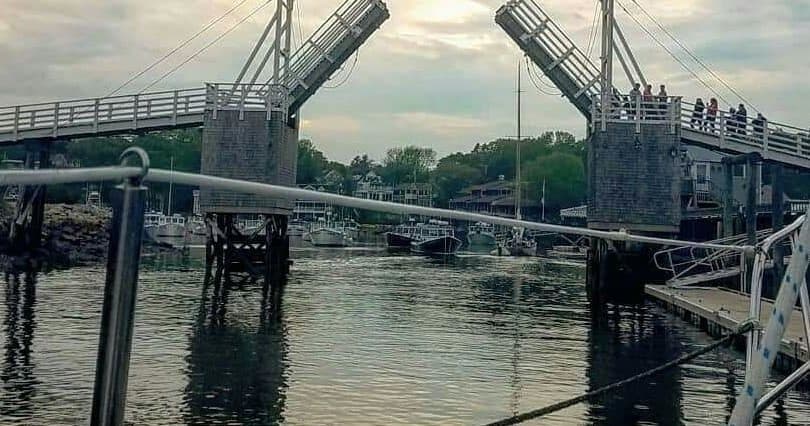 Sailing boat approaching raised drawbridge in coastal harbor at dusk