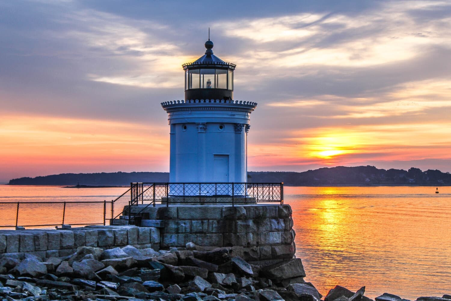 Lighthouse at sunset on rocky coast, scenic seaside viewpoint