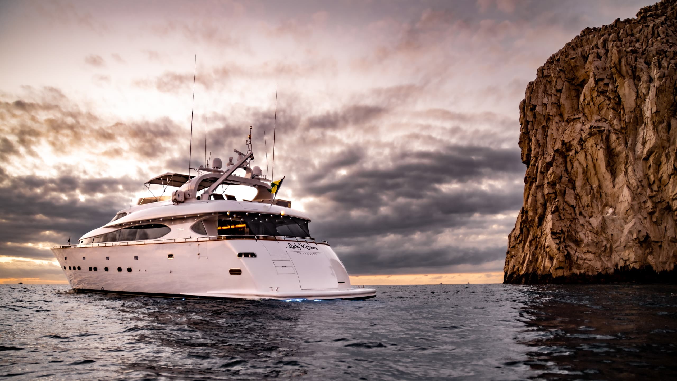 Luxury yacht cruising near sea cliffs at sunset