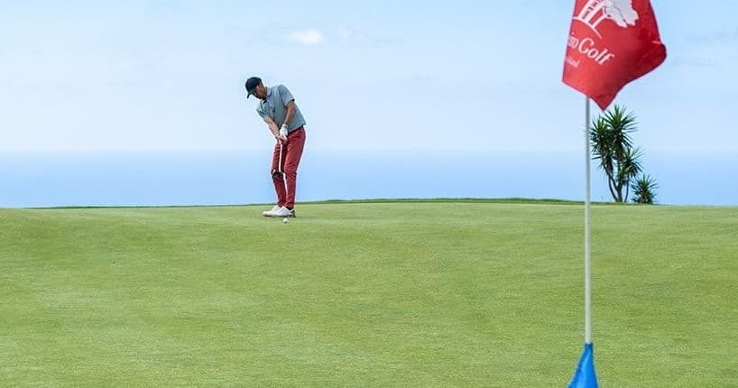 Player chipping toward flag on coastal green with ocean view