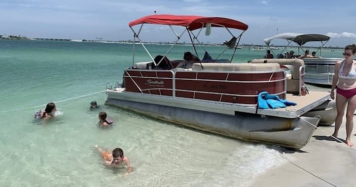 Pontoon boat anchored in clear coastal waters with swimmers