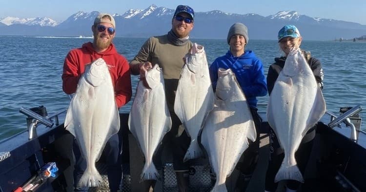 Four anglers holding giant halibut on Alaskan fishing boat