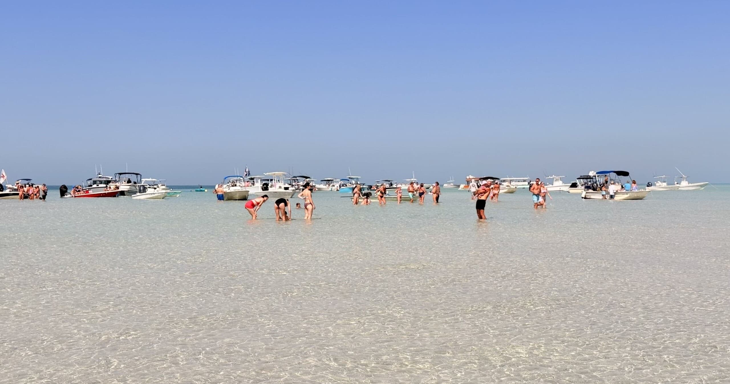 Shallow sandbar beach with anchored boats and wading swimmers