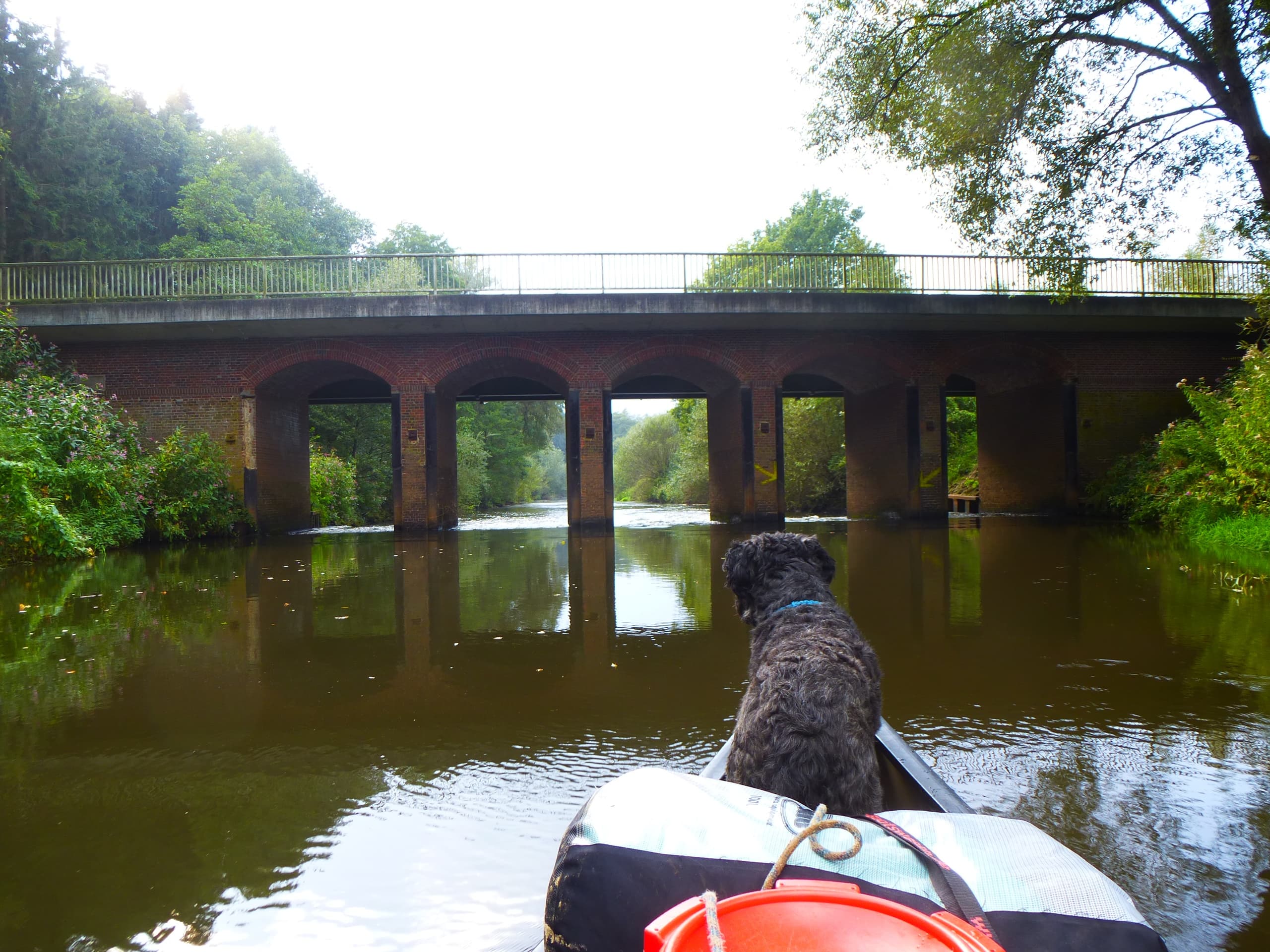 View from canoe with dog approaching stone bridge on river