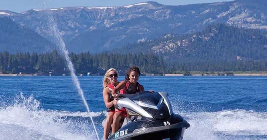 Couple riding red jetski across alpine lake with mountain view