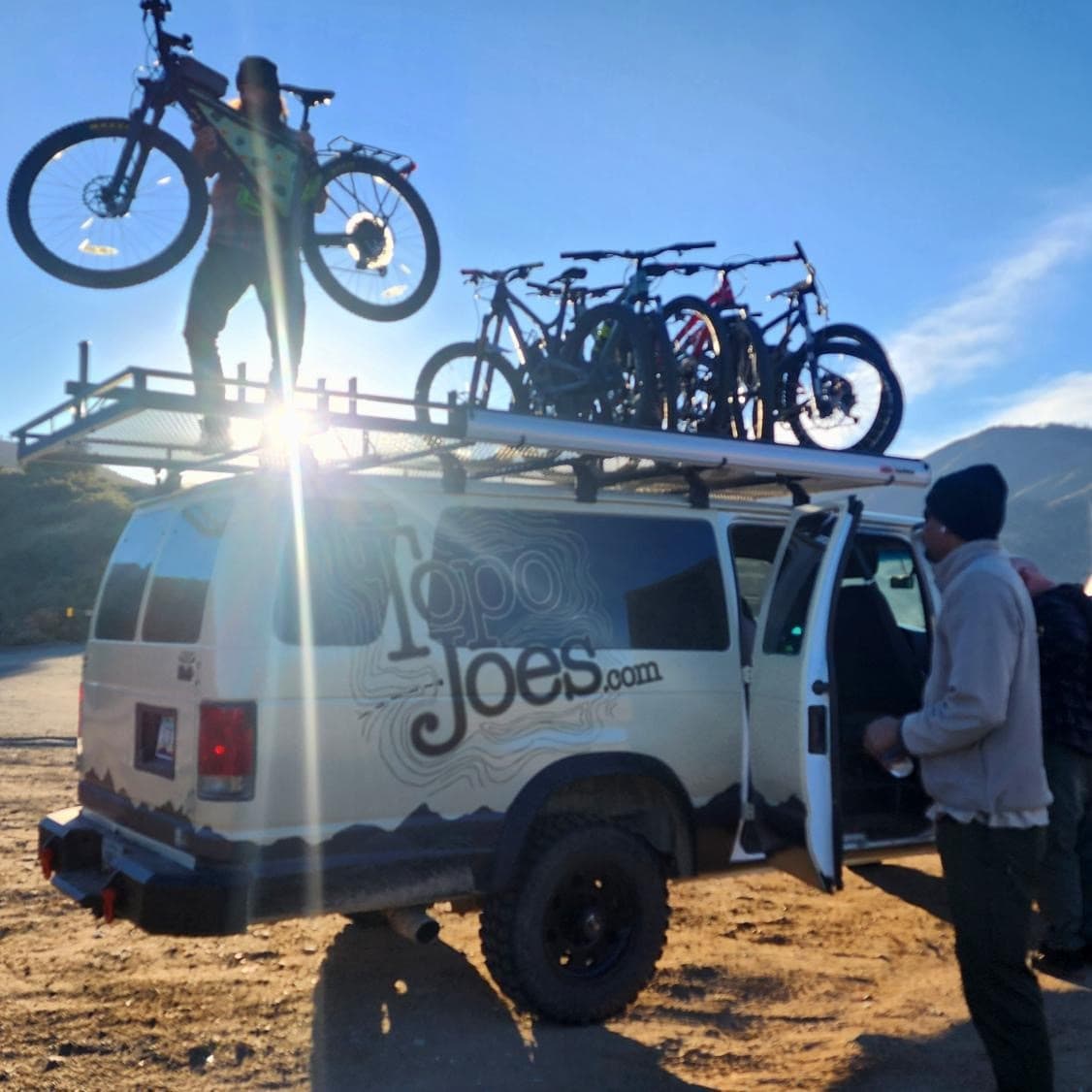 Adventure van with rooftop bikes and sunlight flare at trailhead
