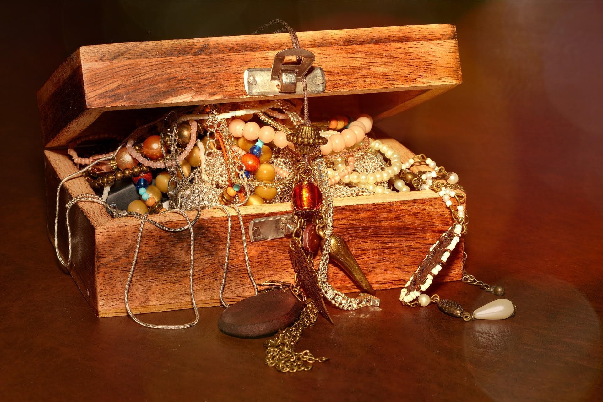 Open wooden treasure chest with assorted jewelry on table