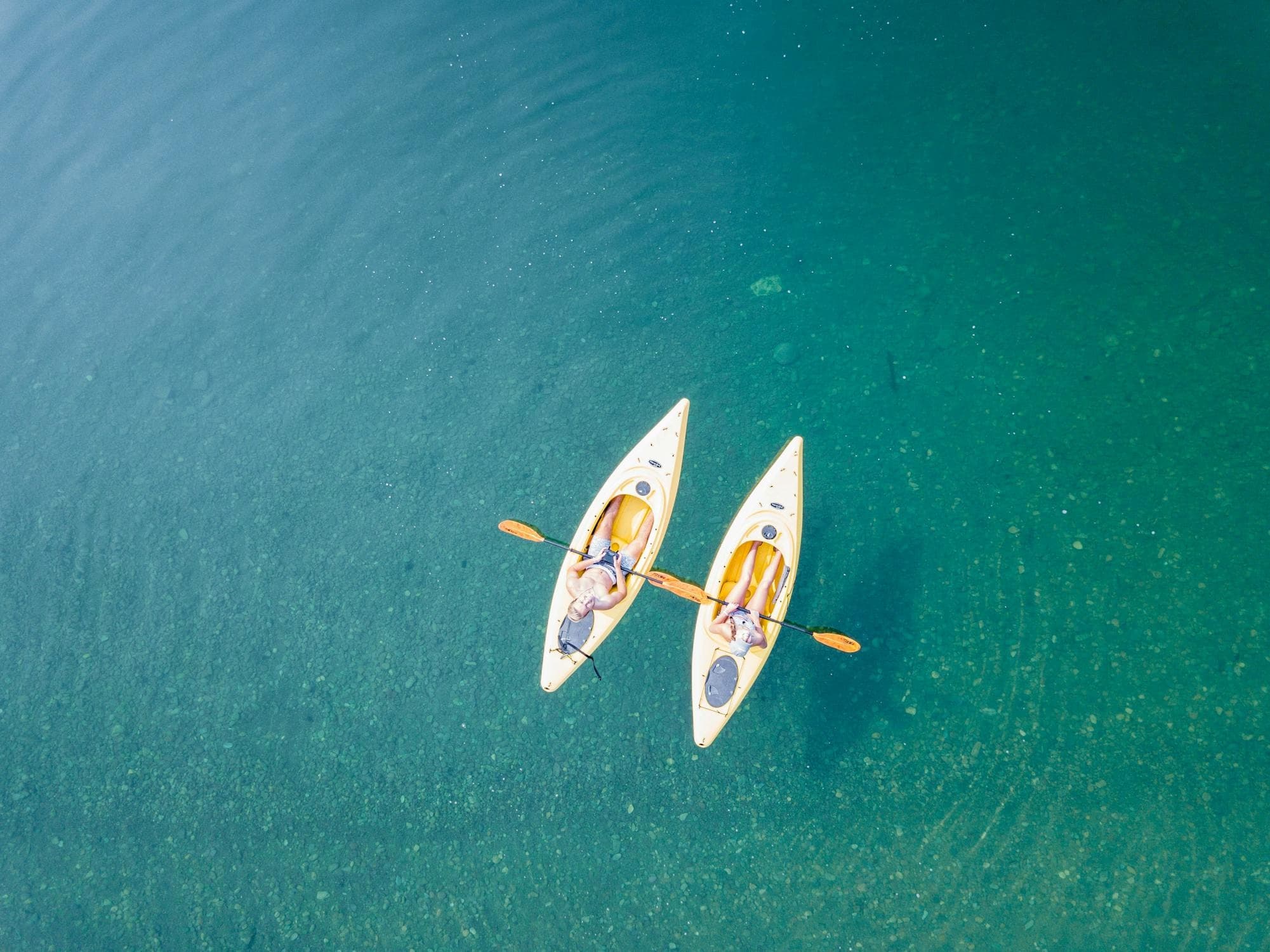 Aerial twin kayakers paddling over clear green coastal waters
