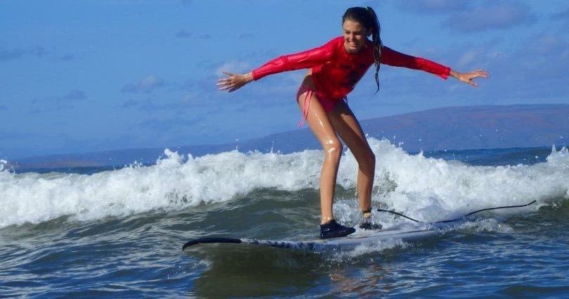 Surfer in red rash guard riding a small breaking wave on reef
