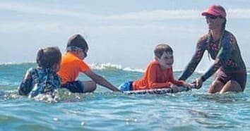 Surf instructor guiding kids on foam board in shallow ocean waves
