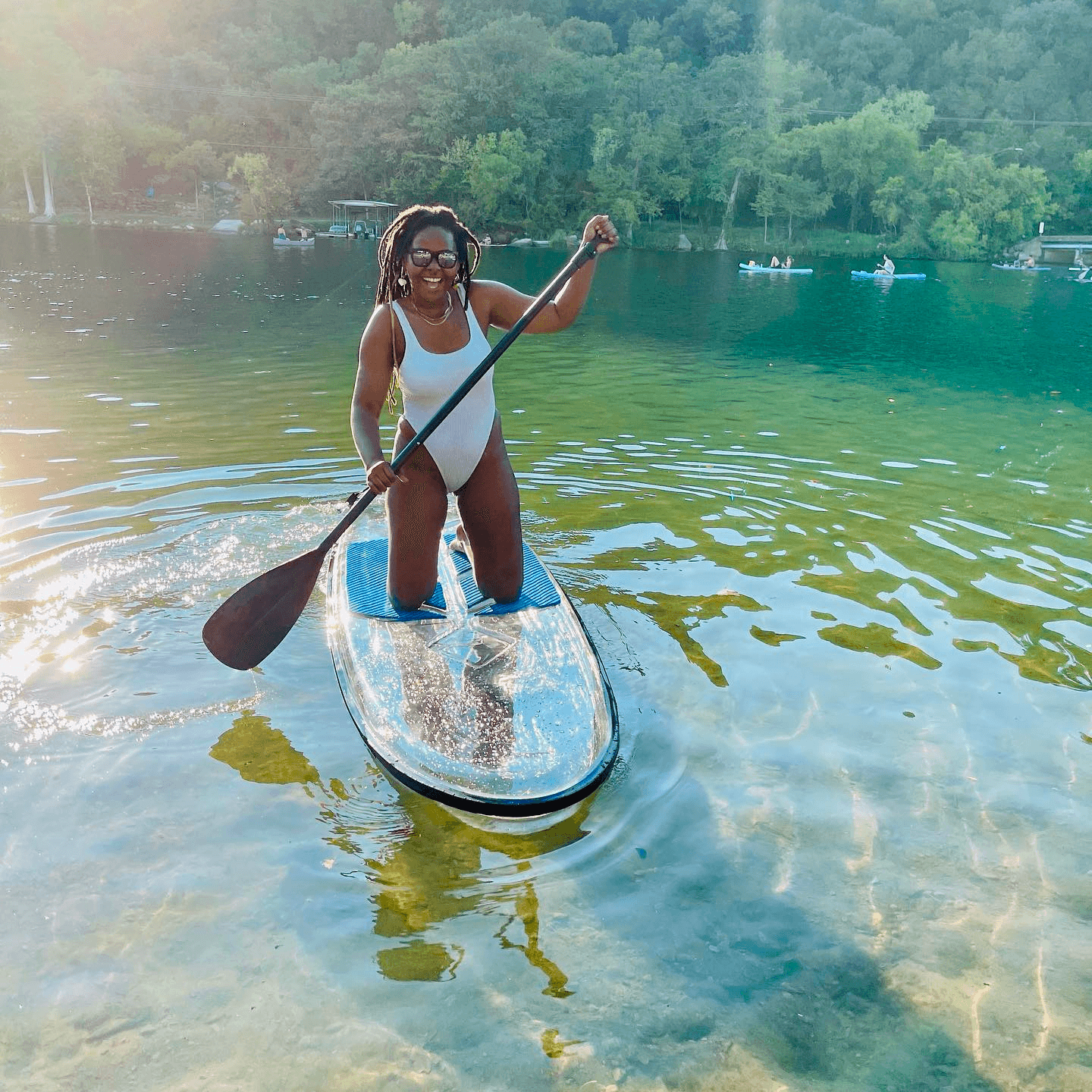 Woman stand-up paddleboarding on clear forest lake at sunset