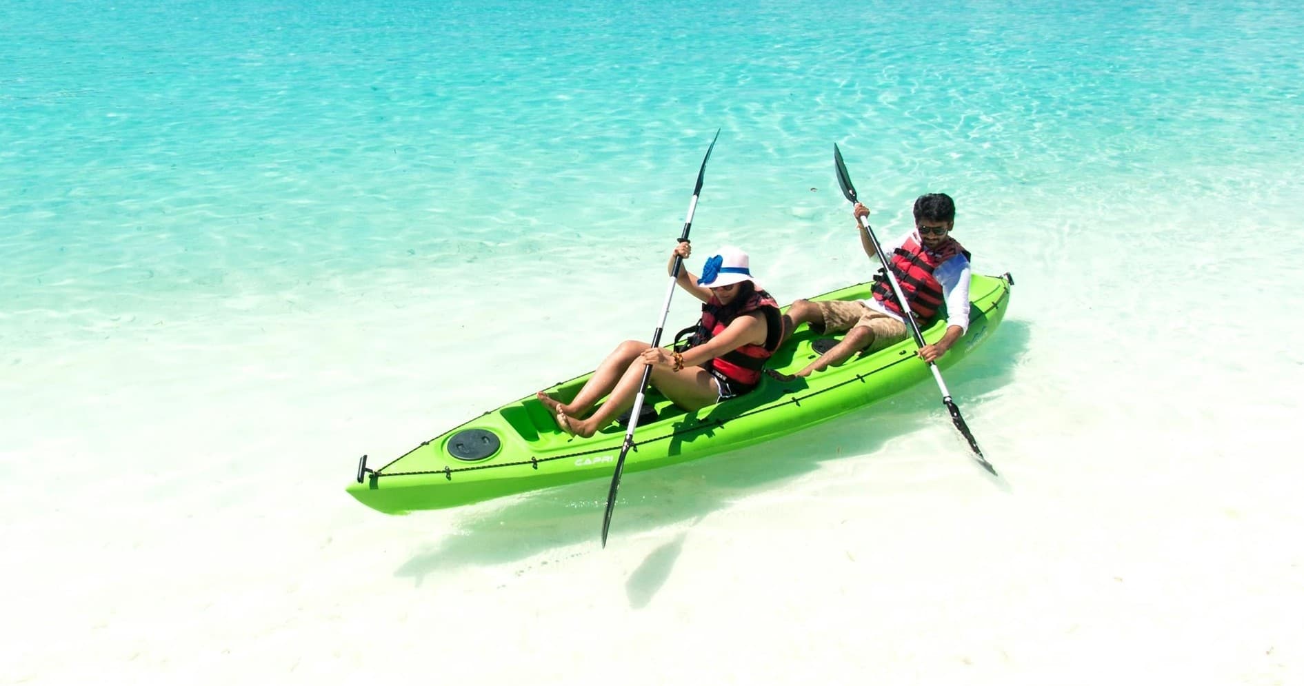 Couple kayaking on shallow white-sand beach in clear water