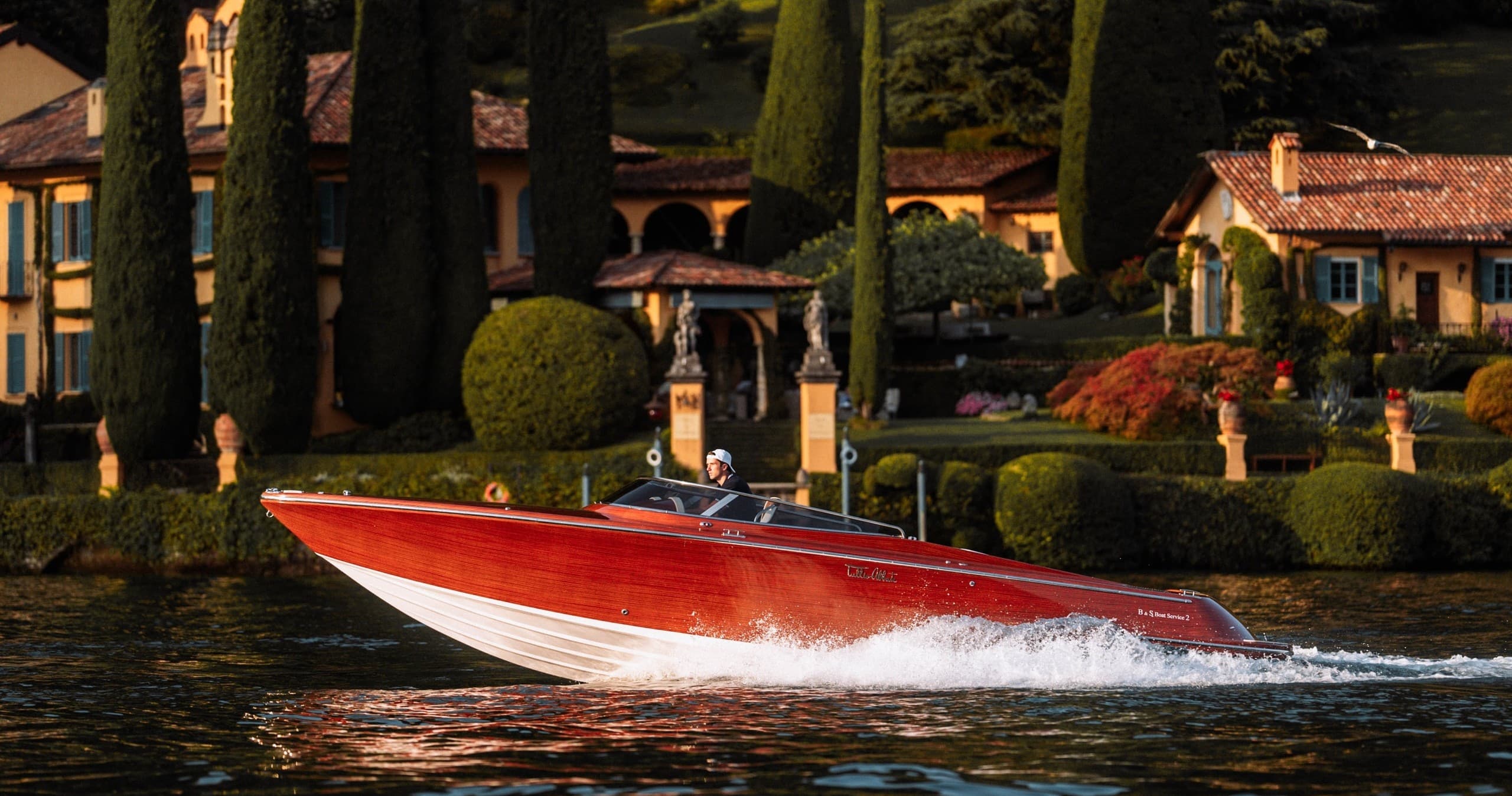 Red speedboat cruising Lake Como shoreline past villas