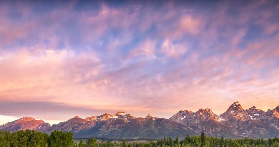 Sunset mountain range panorama over forested valley, dramatic sky
