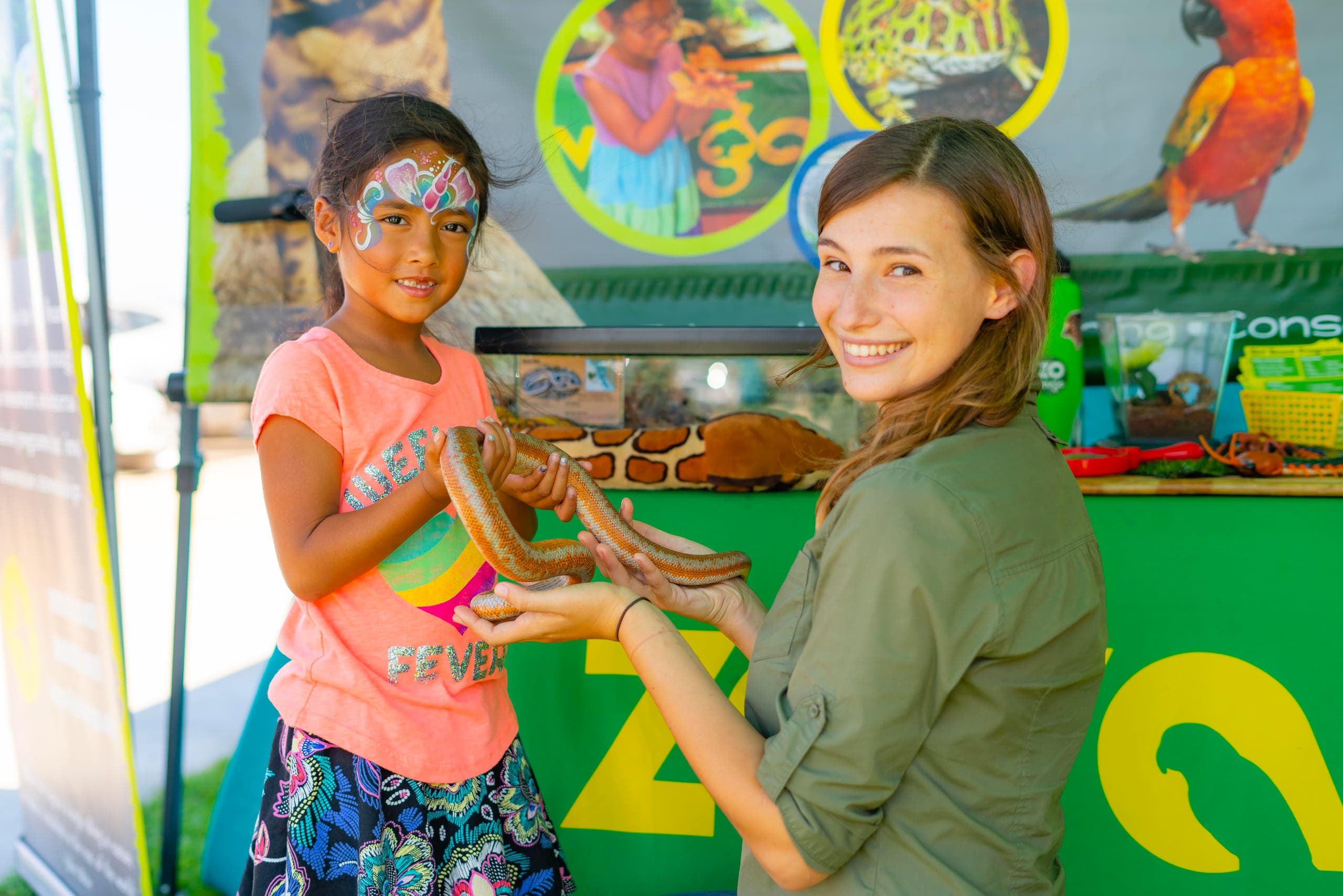 Child and educator holding snake at outdoor wildlife education booth