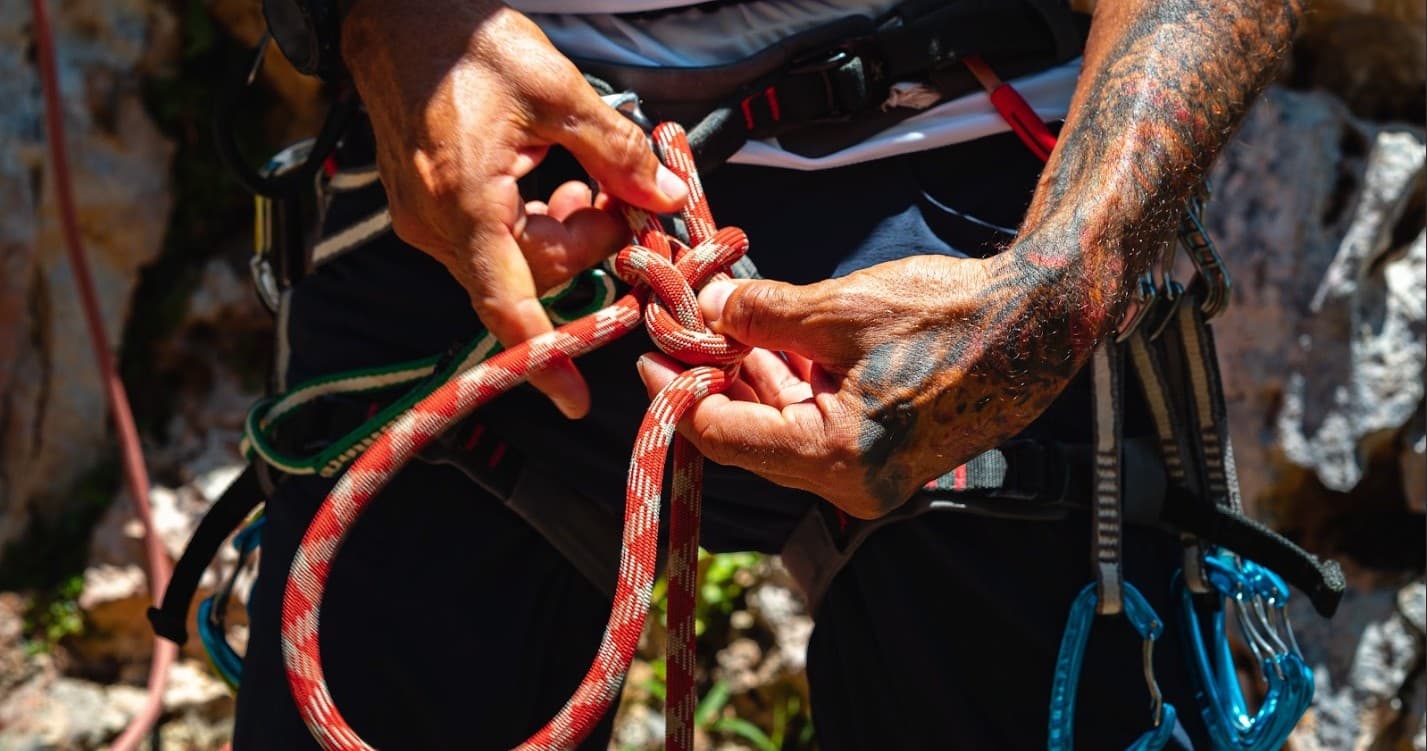 Guide tying climbing rope on scenic outdoor rock climbing trip