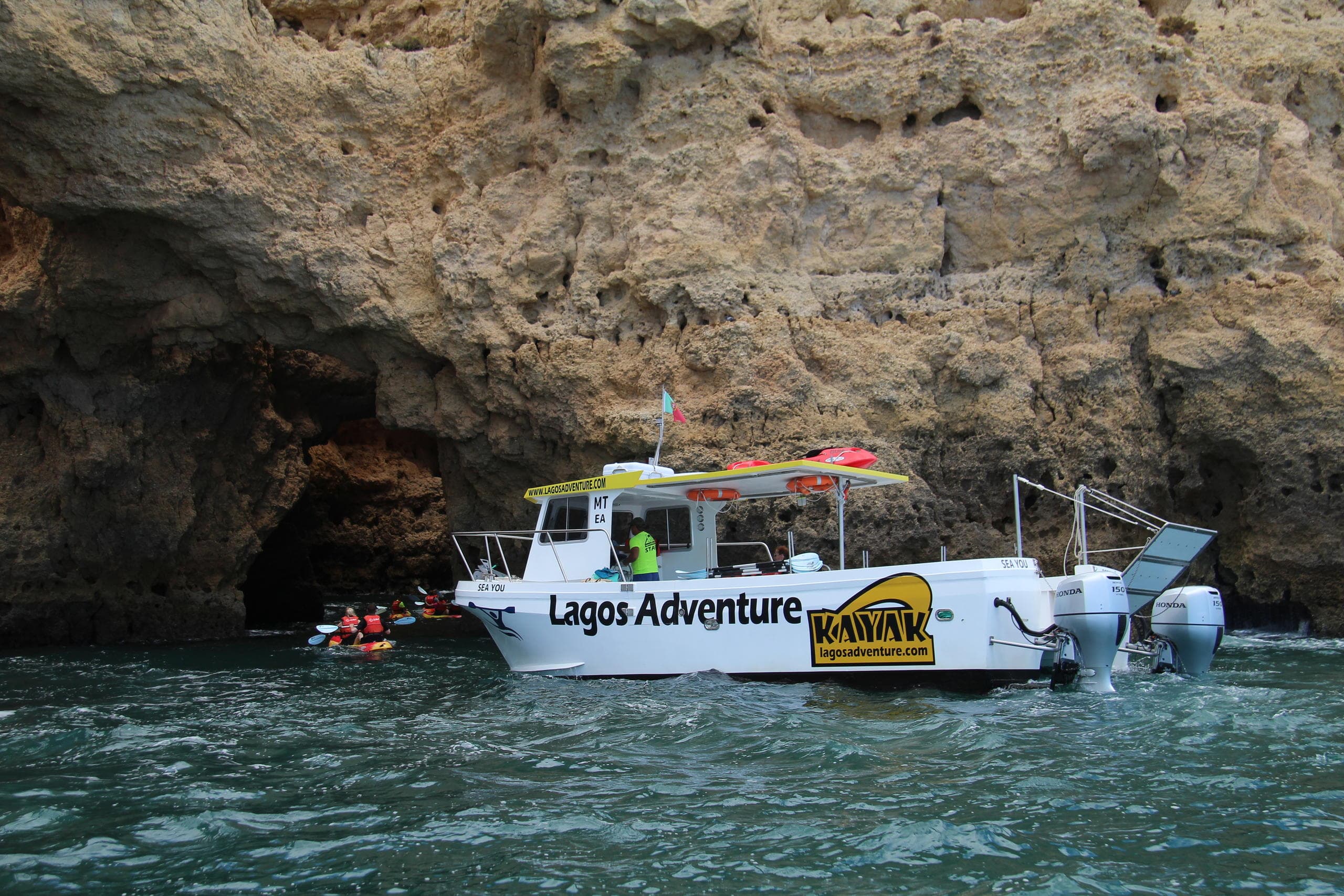 Tour boat with kayaks anchored near Lagos cliffs, Portugal coast