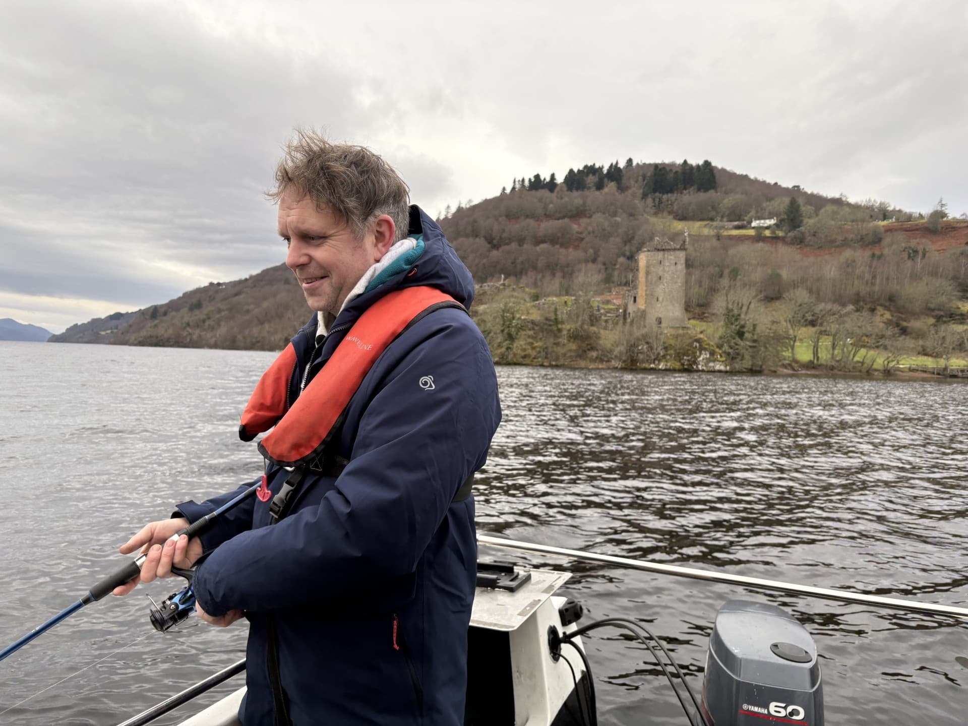 Angler fishing from boat on Loch Ness with castle shore