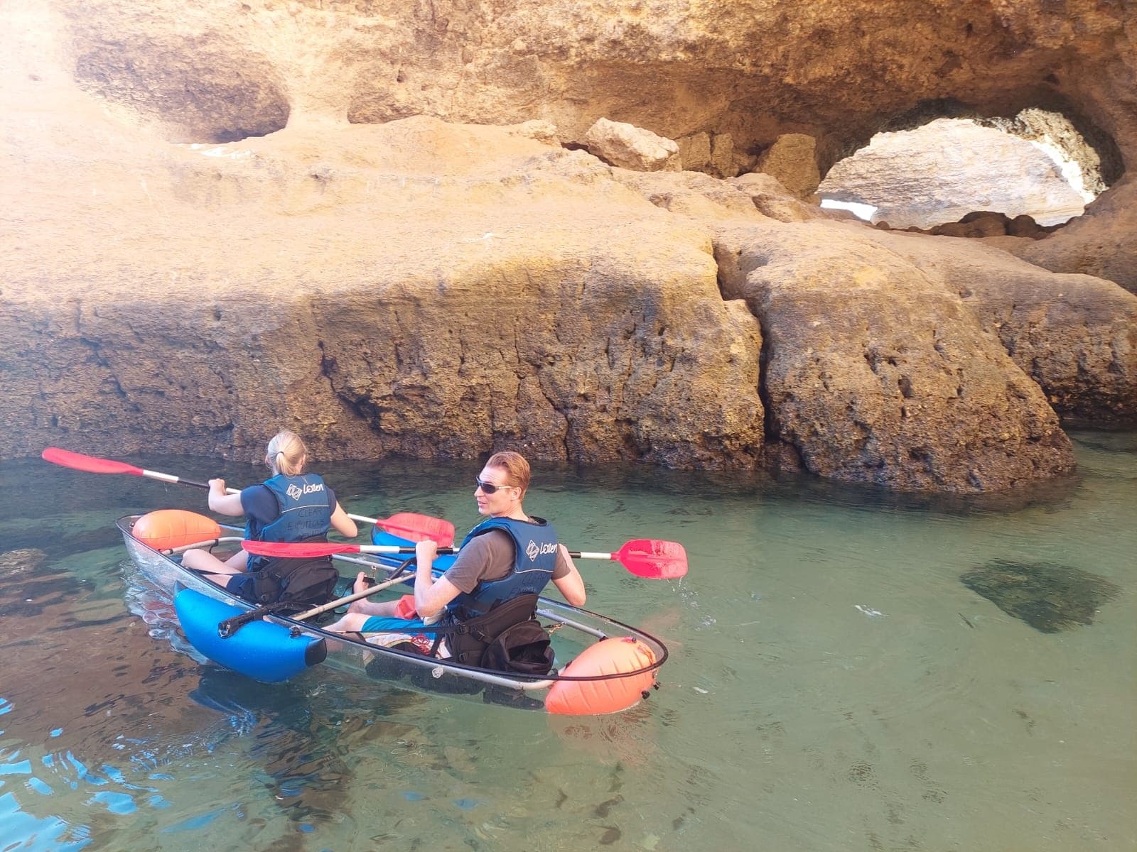 Two kayakers exploring rocky sea cave and coastal rock arch