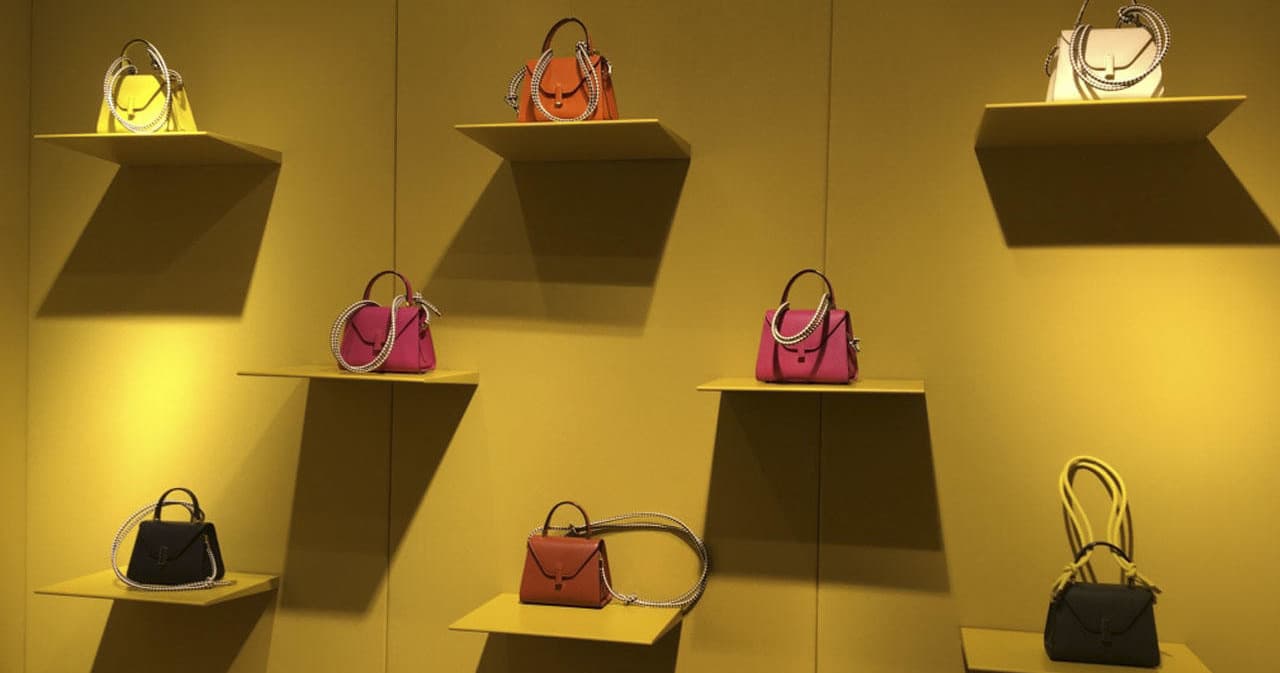 Designer handbags displayed on yellow wall in Milan boutique
