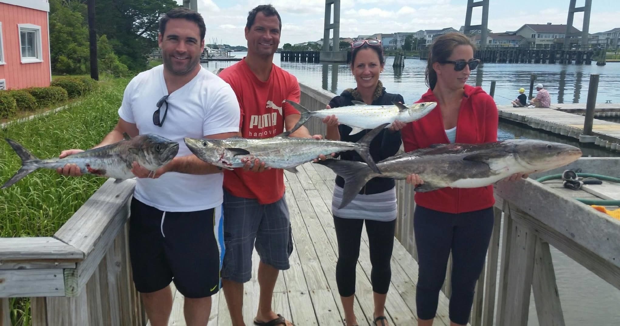 Anglers holding large caught fish on wooden pier after charter