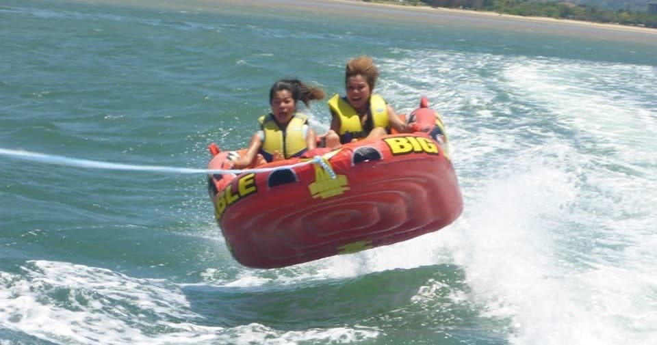 People tubing on choppy ocean waves being towed by speedboat