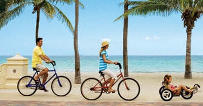 Family cycling along palm-lined beachfront promenade, seaside ride