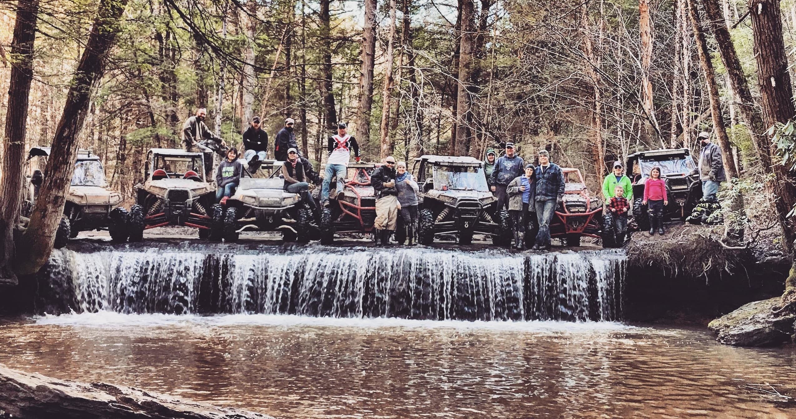Group of UTVs lined at a woodland waterfall and mud crossing