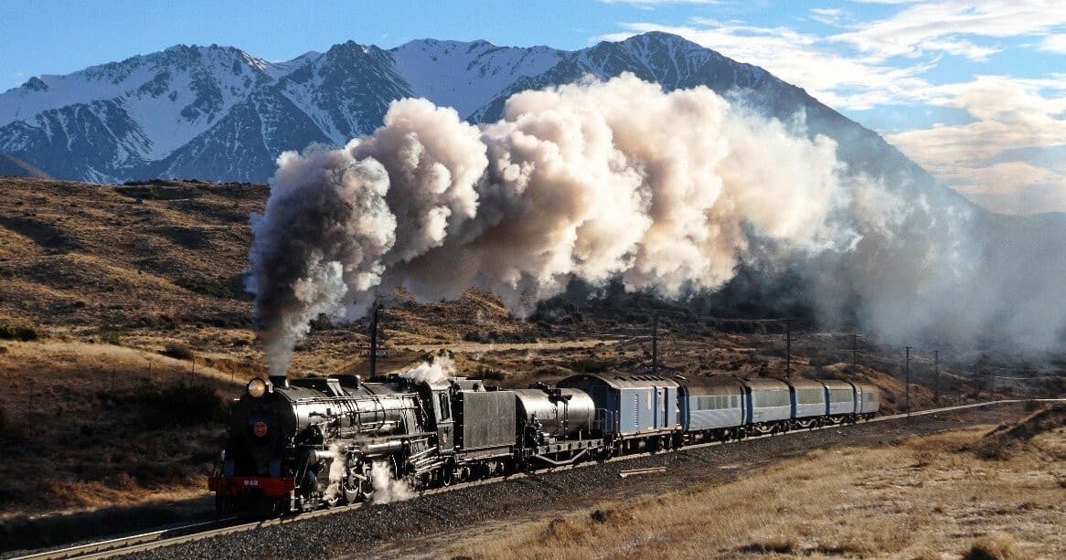 Steam train cruising past snow-capped mountains, scenic tour