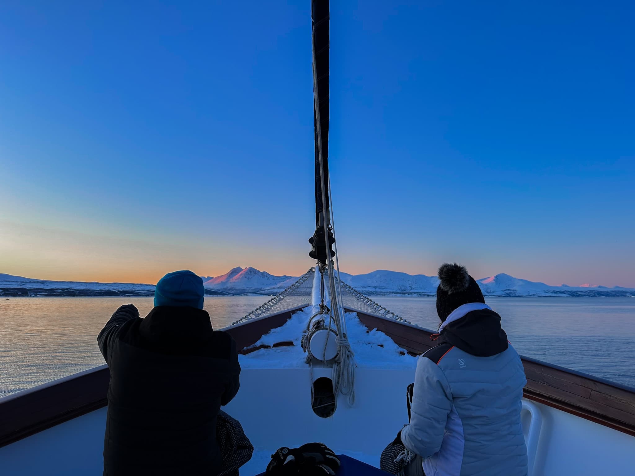 Passengers on bow of sailboat watching sunrise over water
