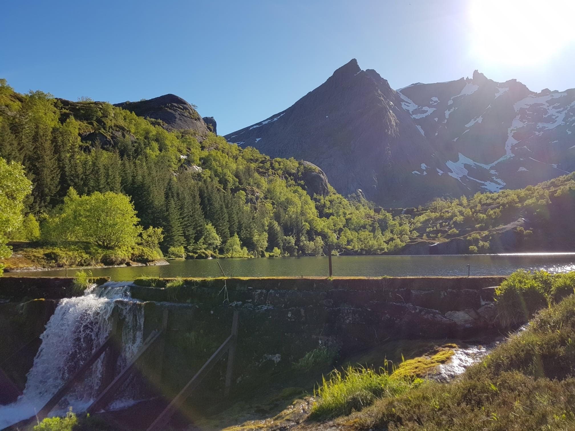 Mountain waterfall and verdant valley under blue sky in Norway