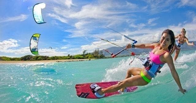 Female kiteboarder carving turquoise lagoon with tropical backdrop