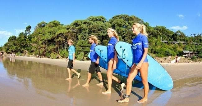 Surfers carrying boards on Lennox Head beach at low tide