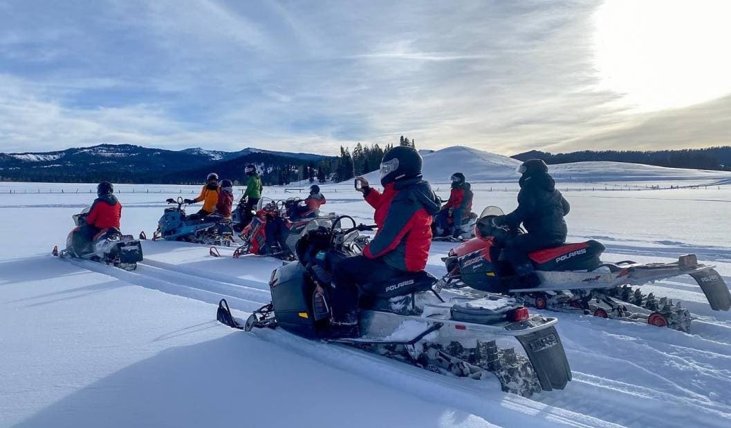 Group snowmobiling on snowy lake at sunrise scenic tour