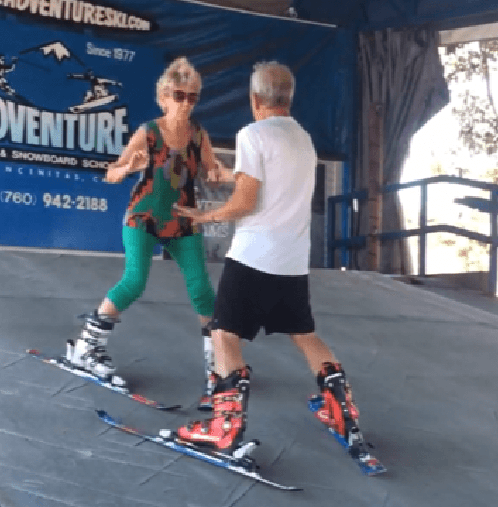 Two adults practicing turns on indoor synthetic ski surface