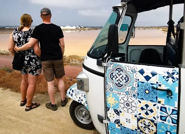 Couple overlooking beach dunes beside decorative tuk-tuk