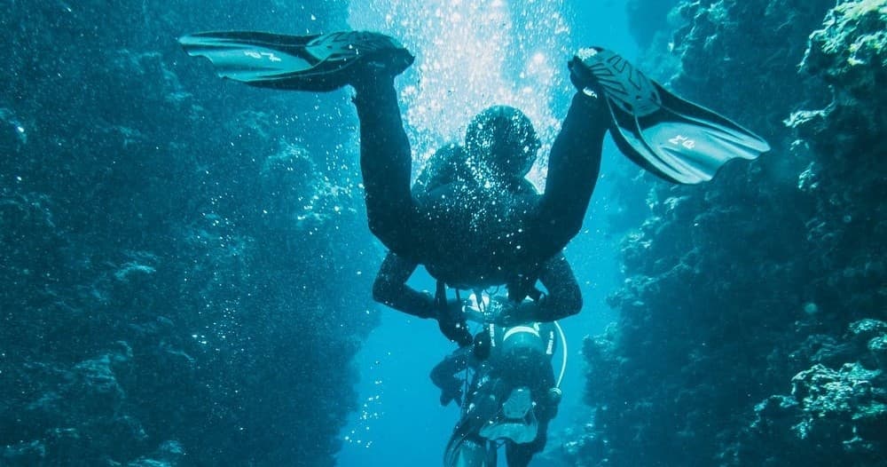 Scuba diver descending through coral canyon in clear blue ocean