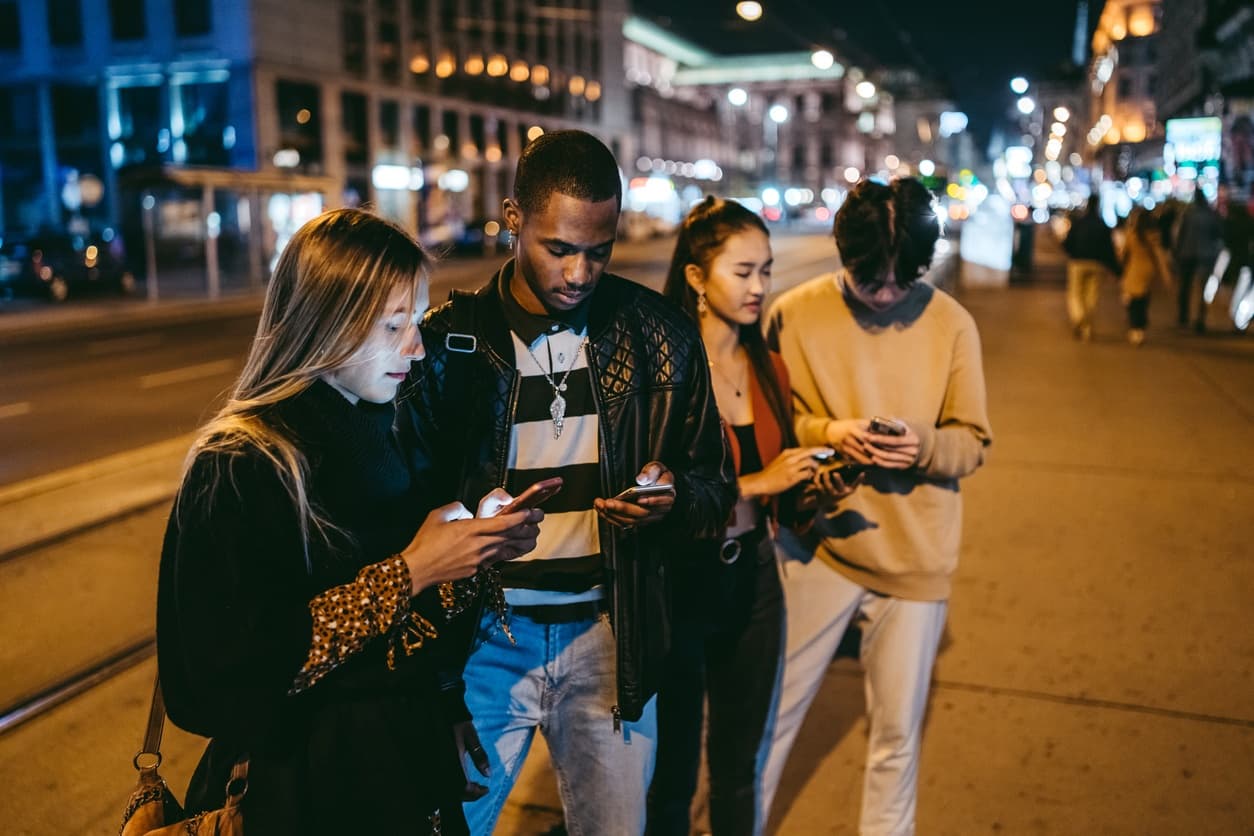 Group of friends on illuminated city street at night using phones