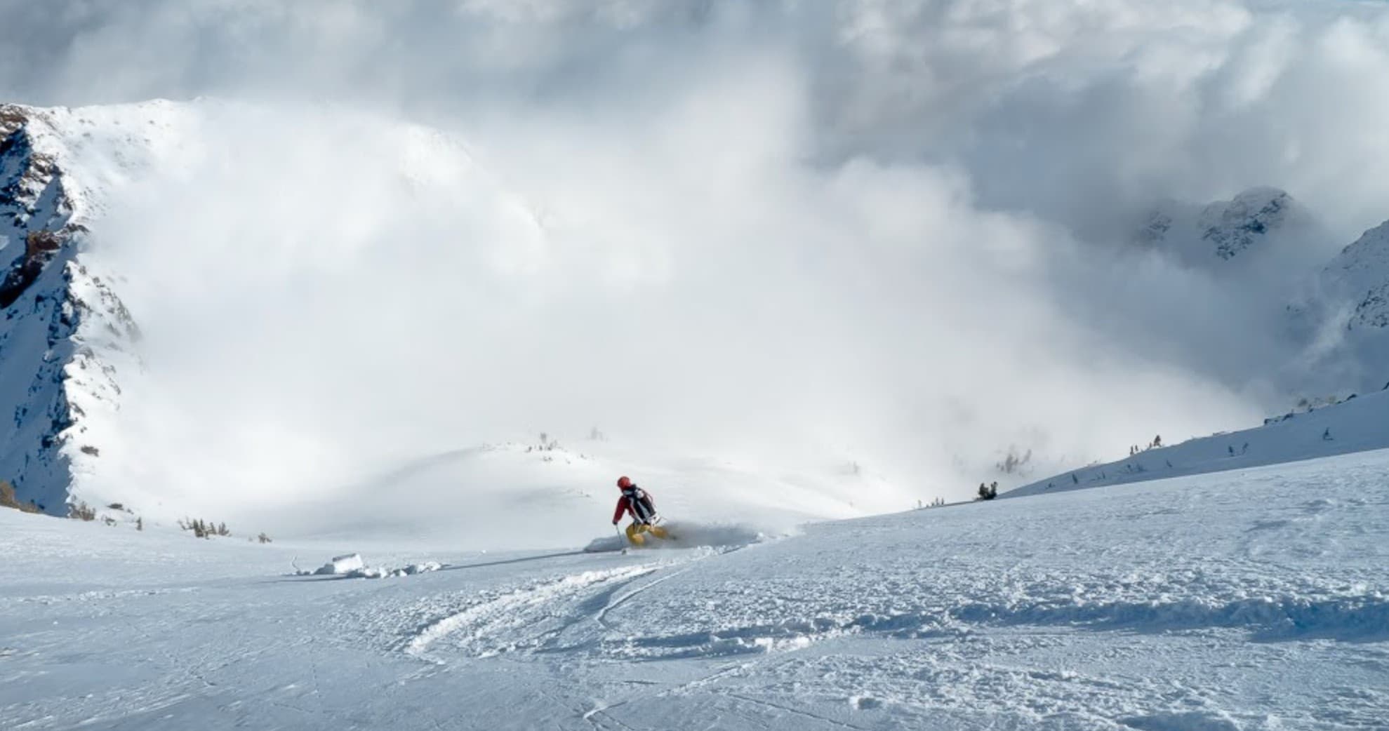 Skier carving deep powder on open snowy slope under cloudy sky