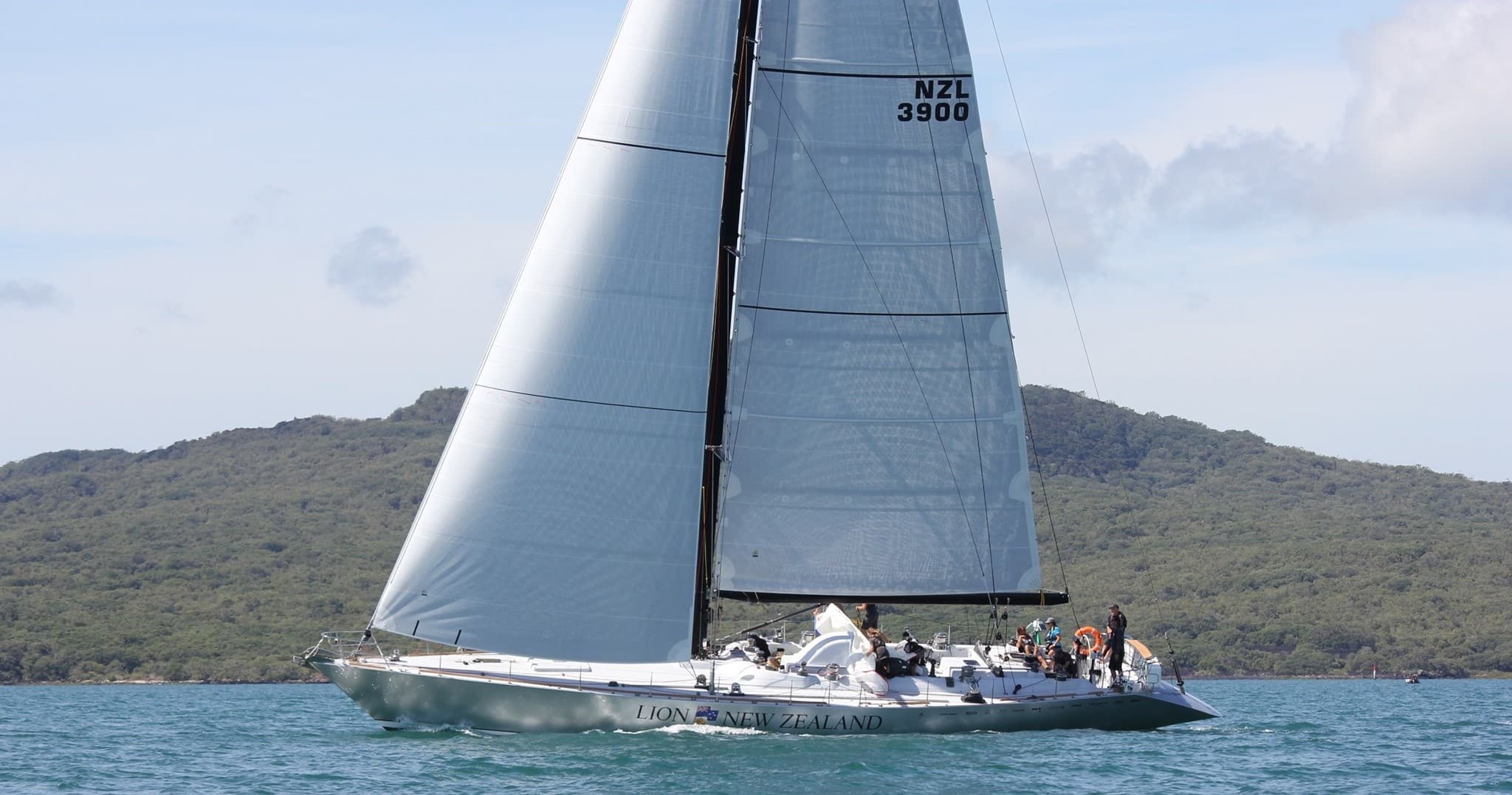 Sleek racing yacht sailing off an island coastline